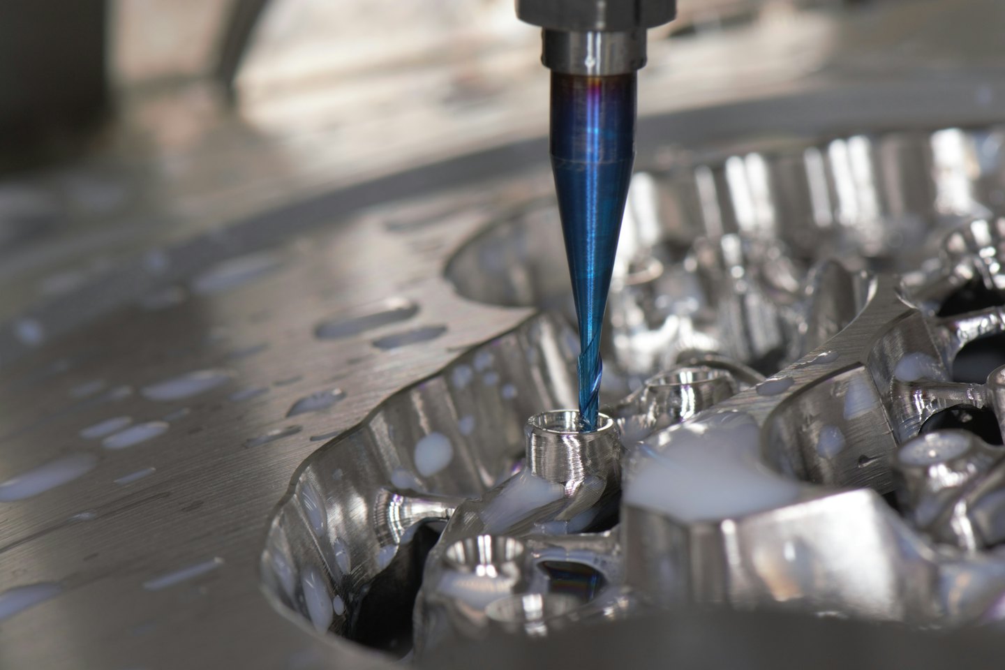 Blauer CNC-Fräser schneidet glänzendes Metallteil mit Kühlschmierstoff-Sprühnebel.