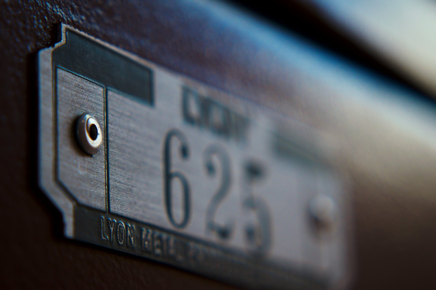 Gebürstete Metallplatte mit der Nummer 625 auf dunklem, strukturiertem Untergrund.